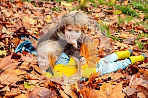 Outdoor autumn portrait of little girl and boy laying in autumn park. Fall leaves relaxing and still life kids concept.
