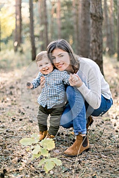 Outdoor autumn portrait of young pretty woman mother posing in autumn pine forest with her lovely cute little son