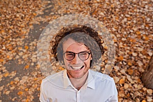 Outdoor autumn shot of smiling handsome young businessman with glasses outdoors. Male student posing against yellow leaves. Smart