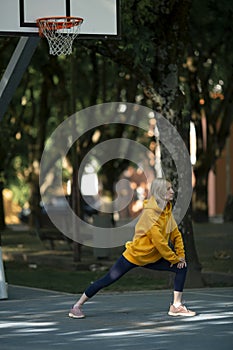 On an outdoor basketball court, a woman exercises.