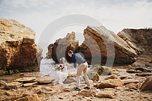 Outdoor beach wedding ceremony near the ocean, romantic happy couple sitting on stones at the beach