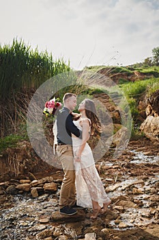 Outdoor beach wedding ceremony, stylish happy smiling groom and bride are kissing near small river. The moment before kiss