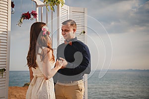 Outdoor beach wedding ceremony, stylish happy smiling groom and bride are standing near wedding altar on the sea shore