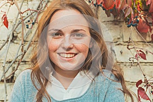 Outdoor beauty. Portrait of smiling young and happy woman with freckles. Background of brick wall with flowers .