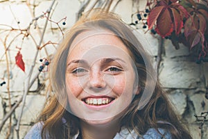 Outdoor beauty. Portrait of smiling young and happy woman with freckles. Background of brick wall with flowers .