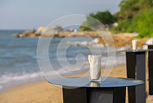 Outdoor cafe or restaurant and glass of water with white napkin on a wooden table on a sandy beach