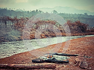 Outdoor camp fireplace near river water, rocks and green grass