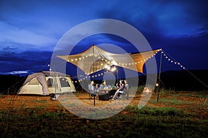 Outdoor camping tent in the forest park, party dinner with friends under tarp or flysheet and warm lighting at night near natural