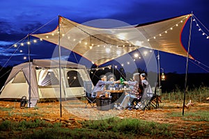 Outdoor camping tent in the forest park, party dinner with friends under tarp or flysheet and warm lighting at night near natural