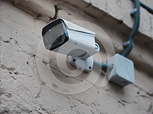 Outdoor CCTV camera mounted on the wall of an old brick house. New camera with protective films on the lens. Video surveillance on