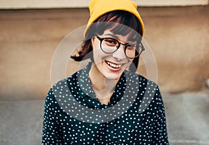 Outdoor close-up portrait of beautiful young woman smiling broadly wearing green shirt with white dots, transparent eyeglasse and