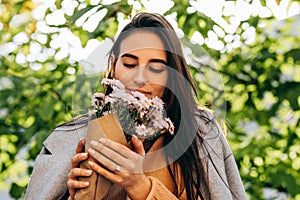 Outdoor close-up portrait of beautiuful young woman smelling the pink flowers on sunny day in the park. Happy female recieved a