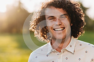 Outdoor close up portrait of happy handsome young male smiling with white toothy smile posing in the city park looking at the