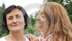Outdoor close up portrait of smiling happy caucasian senior mother with her adult daughter hugging and looking at the