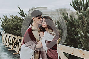 Outdoor close up portrait of young beautiful happy smiling couple bundled up in tartan blanket. Christmas, new year