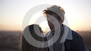 Outdoor close up portrait of young happy stylish couple hugging on the roof at sunset or sunrise. Girl caressing her