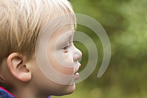 Outdoor closeup portrait of little boy with serious face in profile