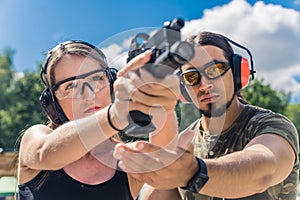 Outdoor closeup shot of focused caucasian skinny woman in protective headphones and glasses aiming at the target