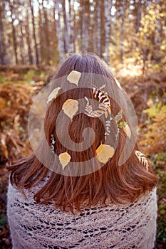 Outdoor conceptual photo of young beautiful lady. Brown hair with autumn fall leaves. Warm autumn, seasonal hair care