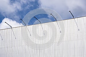 Outdoor corrugated steel advertising billboard structure with spotlights against white clouds on blue sky background