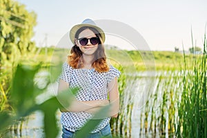 Outdoor country portrait of teenage girl in hat sunglasses near pond in the reeds