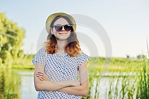 Outdoor country portrait of teenage girl in hat sunglasses near pond in the reeds