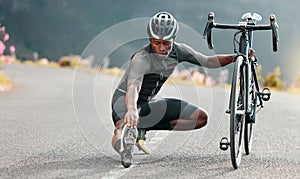 Outdoor, cycling and cyclist doing stretching exercise by his bicycle on road in mountain. Sports, training for fitness