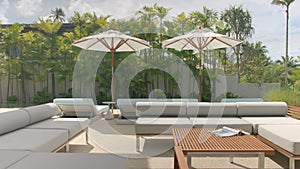 Outdoor deck, terrace with gray deck sofas, table and umbrellas near the swimming pool, next to the beach front