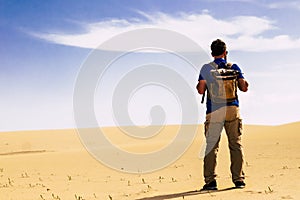 Outdoor desert adventure and alternative tourism and tourist activity with standing man from back with backpack looking a sand