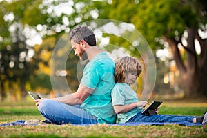 Outdoor distance learning. Father using laptop relax with schooler son holding laptop have fun together. Family with