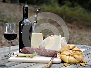 Outdoor eating with bread, cheese, sausage and red wine.