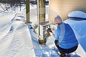 Outdoor electrical panel with an electric meter in countryside in winter, woman takes readings and calculates