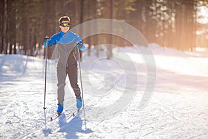 Outdoor exercise in winter in forest, young man trains on cross country skiing on snowy track stadium