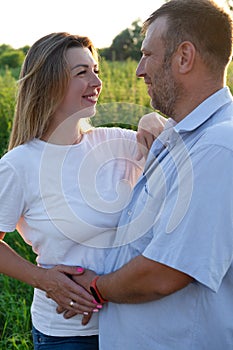 Outdoor family portrait: beautiful young pregnant female and her husband, hands on belly, anticipate child, enjoy