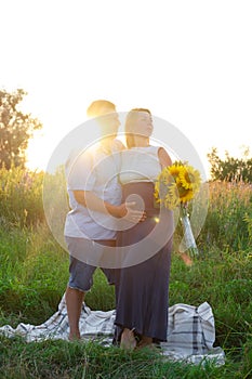 Outdoor family portrait: beautiful young pregnant female and her husband, hands on belly, anticipate child, enjoy