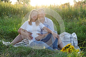 Outdoor family portrait: beautiful young pregnant female and her husband, hands on belly, anticipate child, enjoy