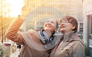 Outdoor family portrait of pension age Mother and her daughter in the city, smiling and looking around. Two generation, happiness