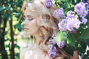 Outdoor fashion beautiful young woman surrounded by lilac flowers summer. Spring blossom lilac bush. Portrait of a girl blond