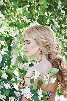 Outdoor fashion beautiful young woman surrounded by lilac flowers summer. Spring blossom lilac bush. Portrait of a girl blond