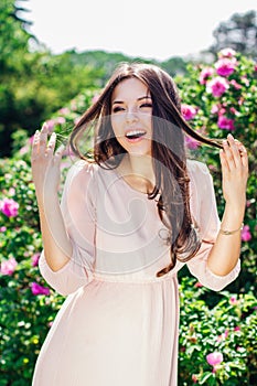 Outdoor fashion photo of beautiful young happy smiling woman surrounded by flowers. Spring blossom