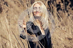 Outdoor fashion photo of young beautiful lady in autumn landscape with dry flowers.