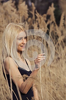 Outdoor fashion photo of young beautiful lady in autumn landscape with dry flowers.