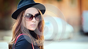 Outdoor fashion portrait of smiling young woman wearing trendy black hat and big retro sunglasses