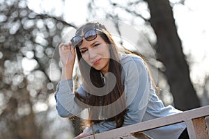 Outdoor fashion portrait of young beautiful fashionable girl with sunglasses, standing by the bridge