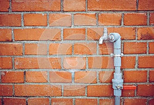 Outdoor faucet water tap with gray PVC pipe and red valve on red brick wall background texture, water saving concept