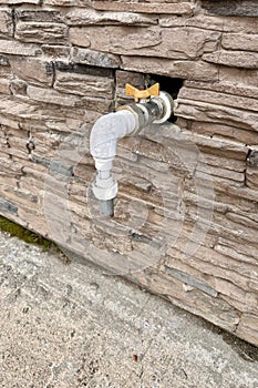 Outdoor faucet water tap with white PVC pipe and reed valve on light brick wall background texture