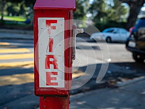 Outdoor fire alarm call box at urban intersection, fire in bold font