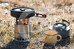 Outdoor food preparation. closeup of frying pan portable wood stove, teapot and metal mug in mountains