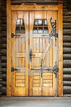 Outdoor front view of a naturally wood finished door entrance. Rustic traditional decorative pattern with iron hinge fittings.