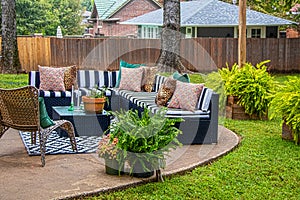 Outdoor furniture - striped sectional on round patio with area rug and chair and ferns with trees and neighboring houses in photo